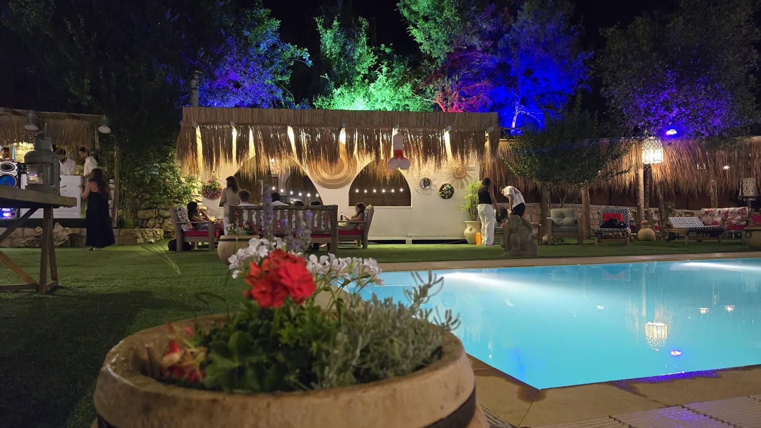 Guests enjoying a vibrant nighttime pool party at Kaya's Resort, an exclusive event venue near Beit Chabab, Lebanon, with colorful lights illuminating the trees.